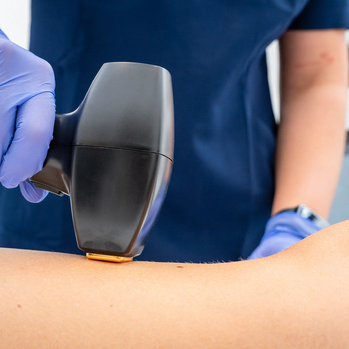 Cosmetic nurse performing laser hair removal treatment on the leg of a patient