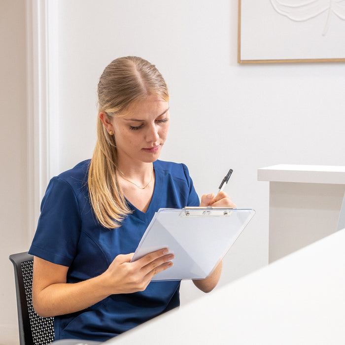 Nurse in navy scrubs completing client paperwork on a clipboard at clinic reception.